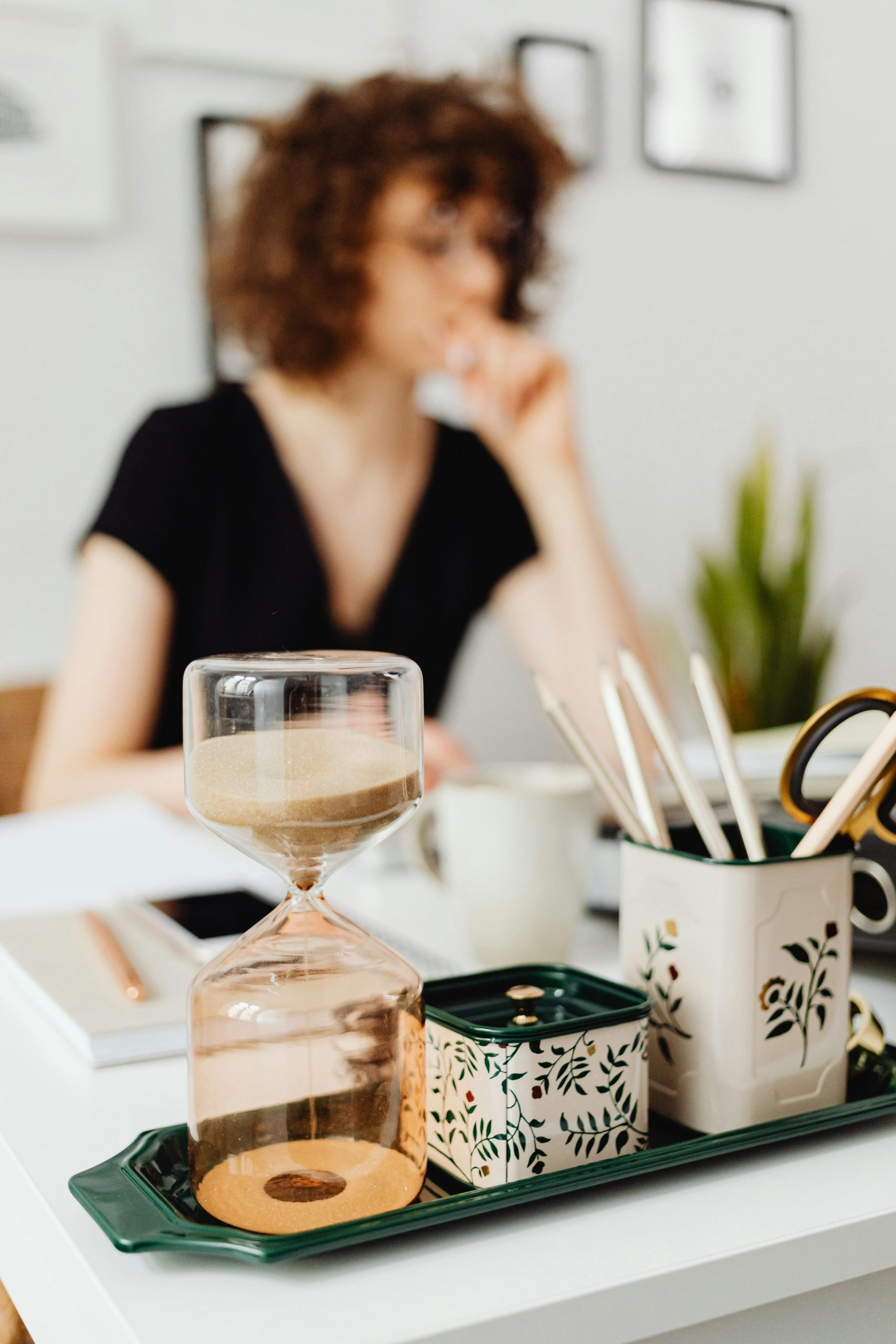 Sablier en premier plan sur le bureau d'une femme en second plan flouté.

Photo de Karola G: https://www.pexels.com/fr-fr/photo/femme-bureau-etre-assis-tasses-7681222/