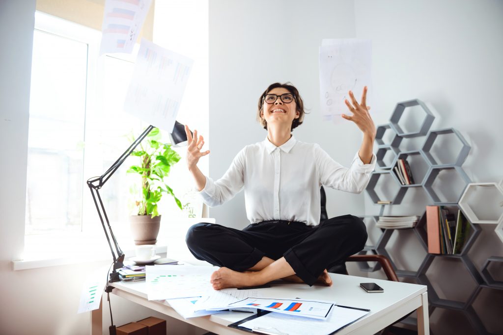 Femme heureuse jetant des papiers assise sur son bureau. Gestion administrative simplifiée